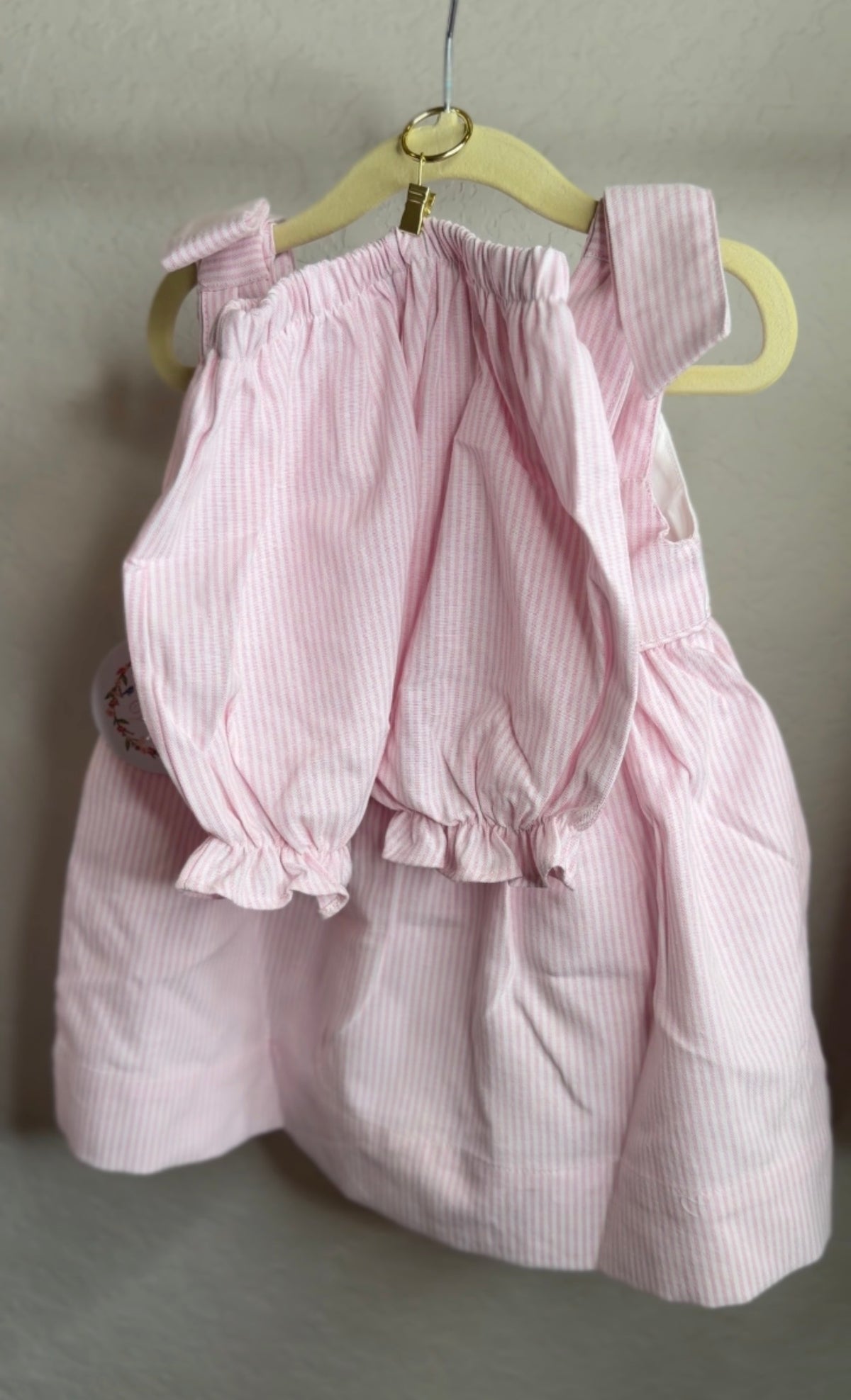 Pink striped dress on a hanger against a plain background