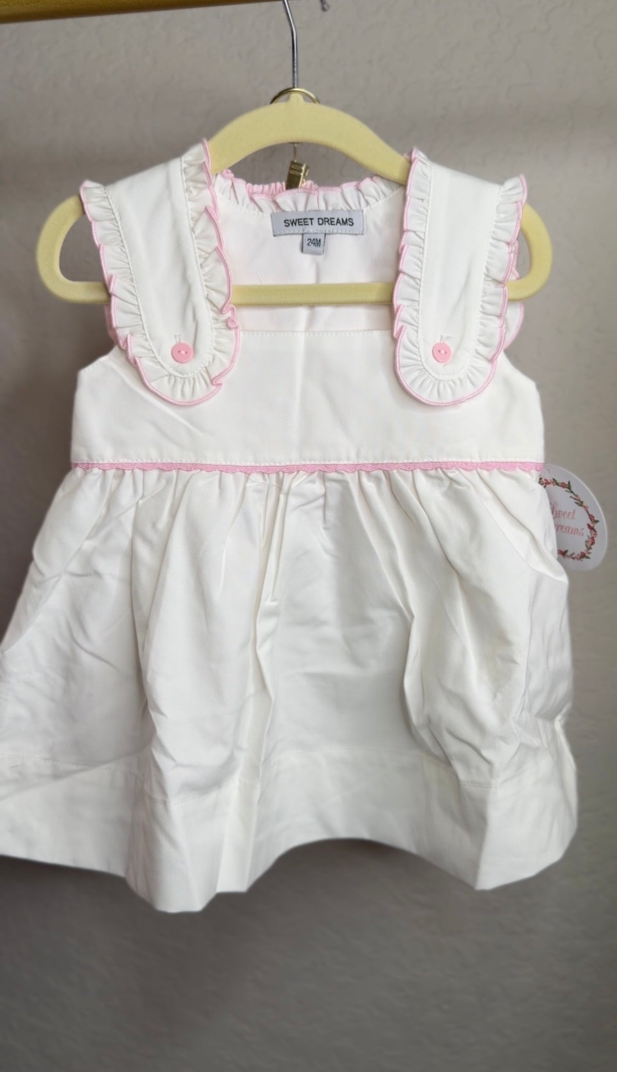 White with pink ruffle trim bloomer set hanging on a hanger in front of a blank wall
