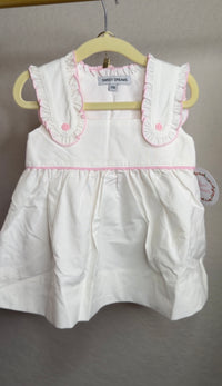 White with pink ruffle trim bloomer set hanging on a hanger in front of a blank wall