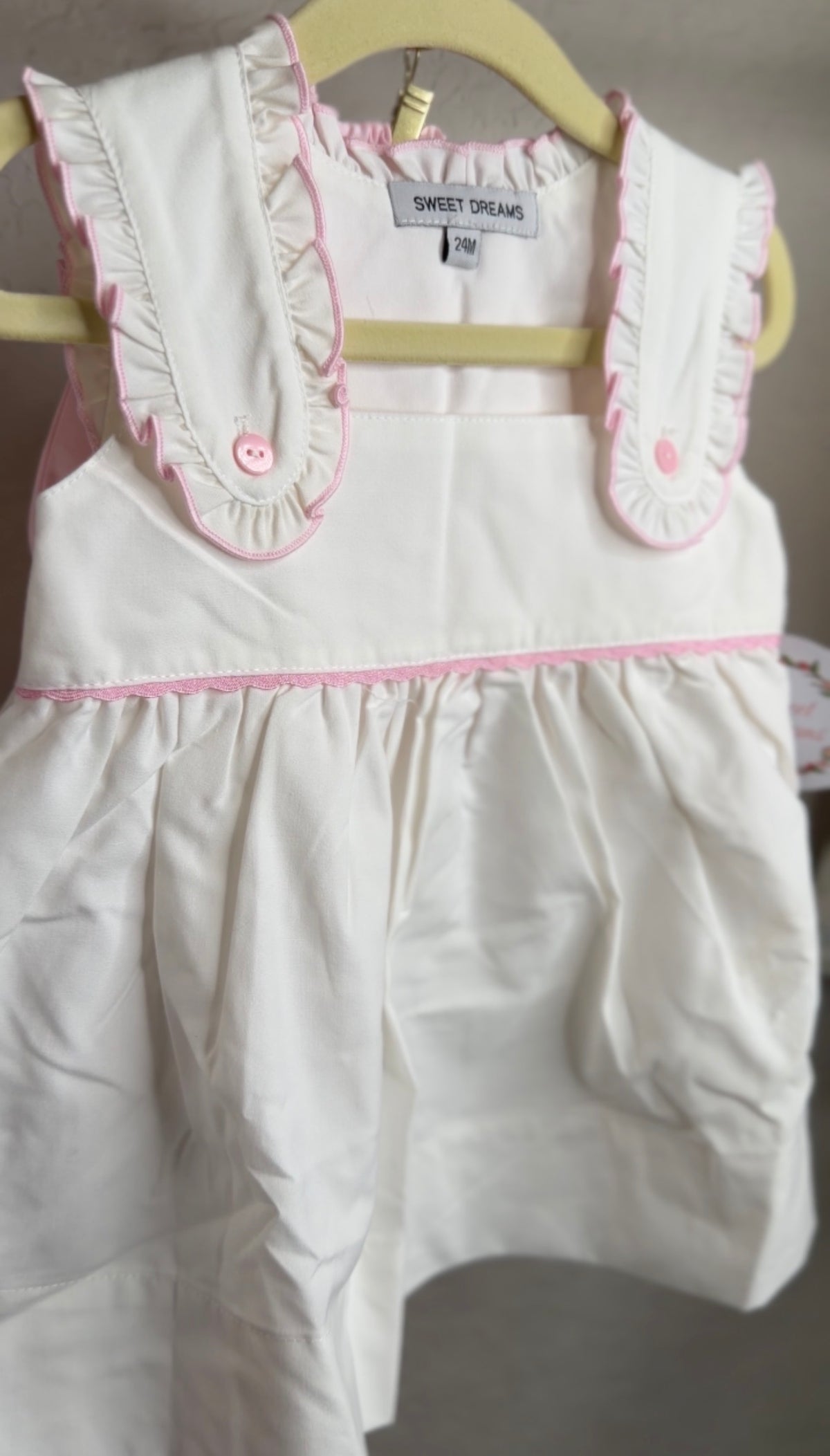 White with pink ruffle trim bloomer set hanging on a hanger in front of a blank wall