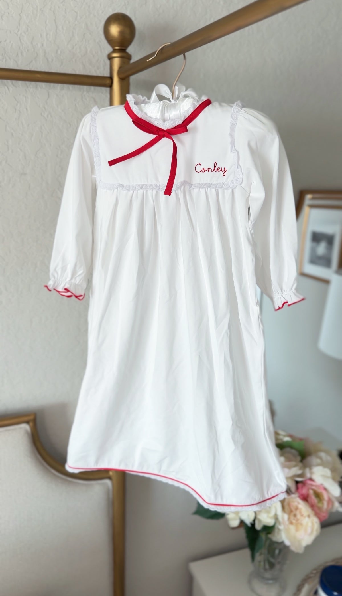 White pima cotton nightgown with red ribbon bow, hanging with embroidered name