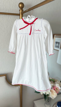White pima cotton nightgown with red ribbon bow, hanging with embroidered name