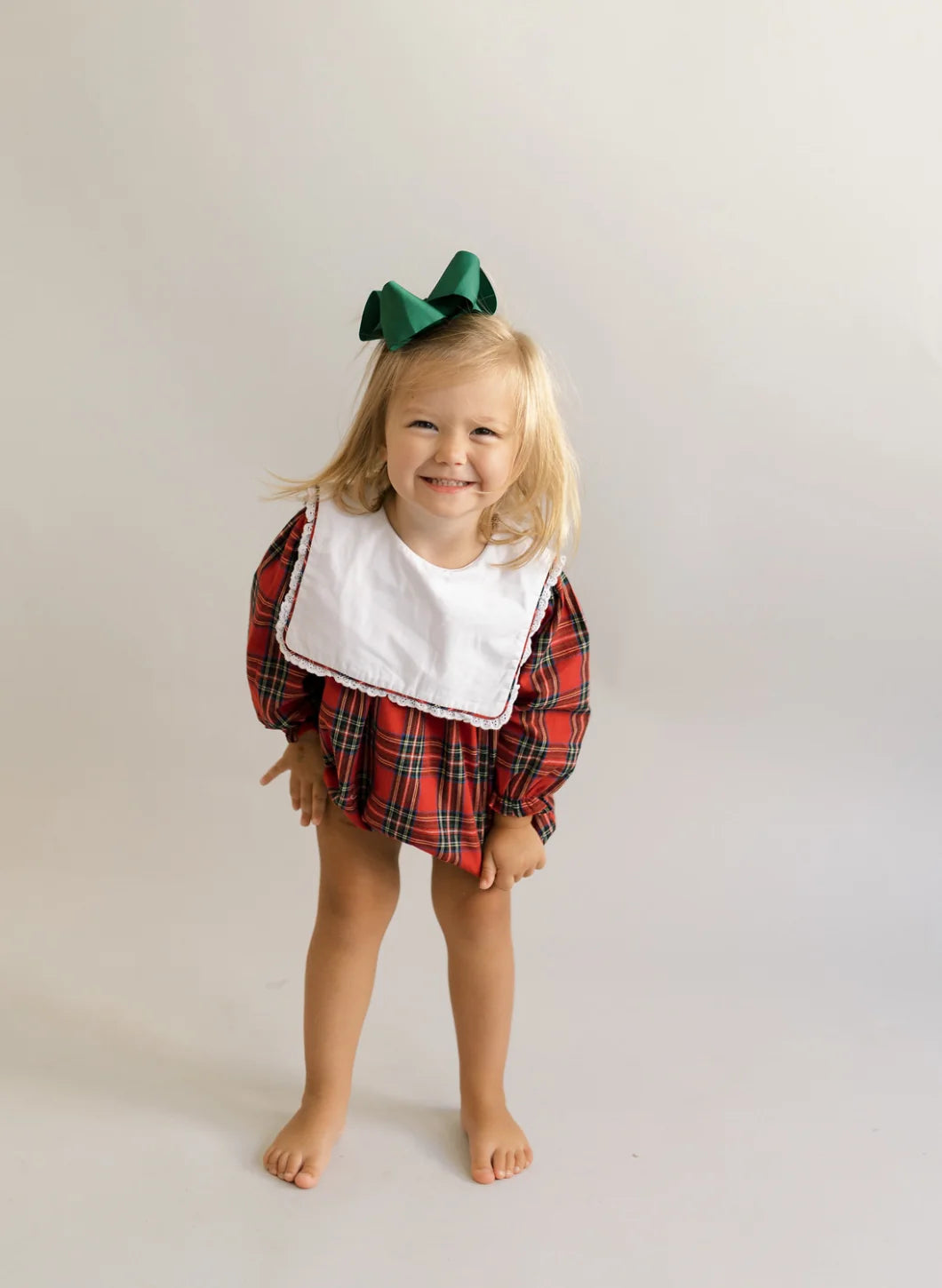 Toddler in red and green plaid bubble romper with white collar and green bow
