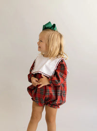 Toddler in red and green plaid bubble romper smiling, side view