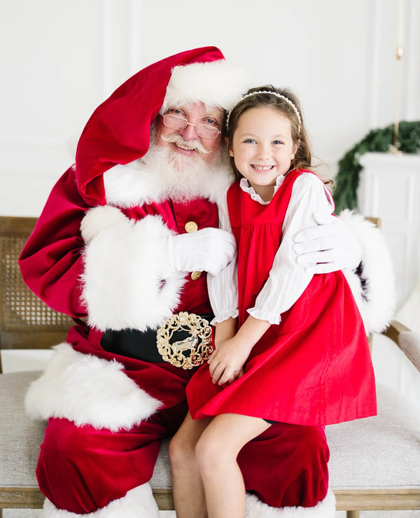 Girl in red corduroy dress with white puff-sleeve blouse sitting with Santa