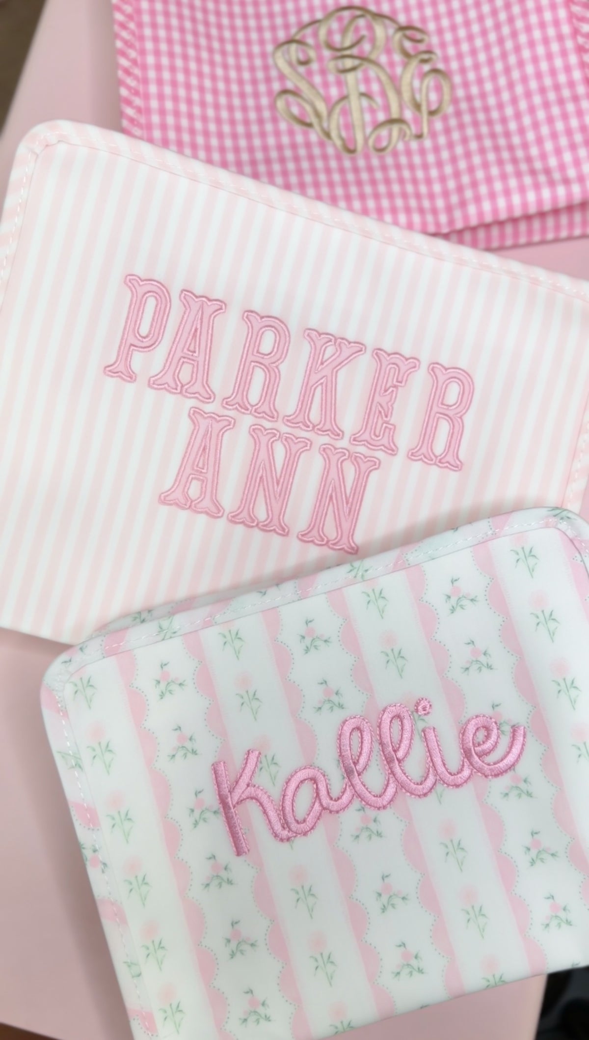 Pink Pimlico stripe TRVL Roadie pouch embroidered with 'PARKER ANN' in block letters, shown with other monogrammed pouches