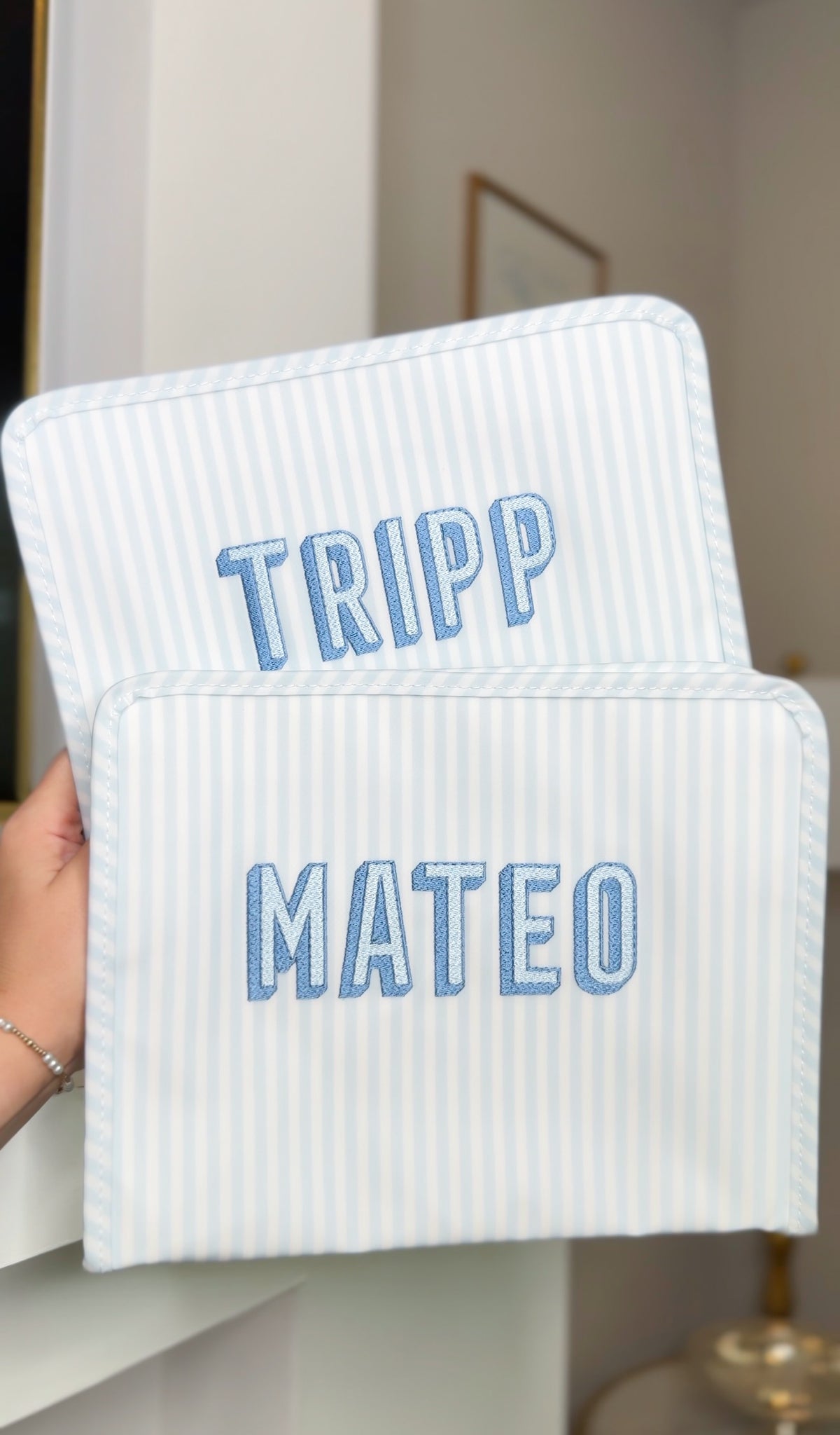 Two blue and white striped TRVL Roadie pouches embroidered with 'TRIPP' and 'MATEO' in block letters