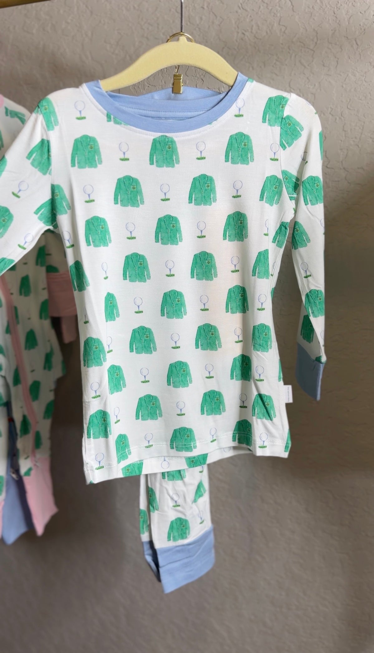 Children's long-sleeve shirt with green coat pattern on a hanger against a neutral background