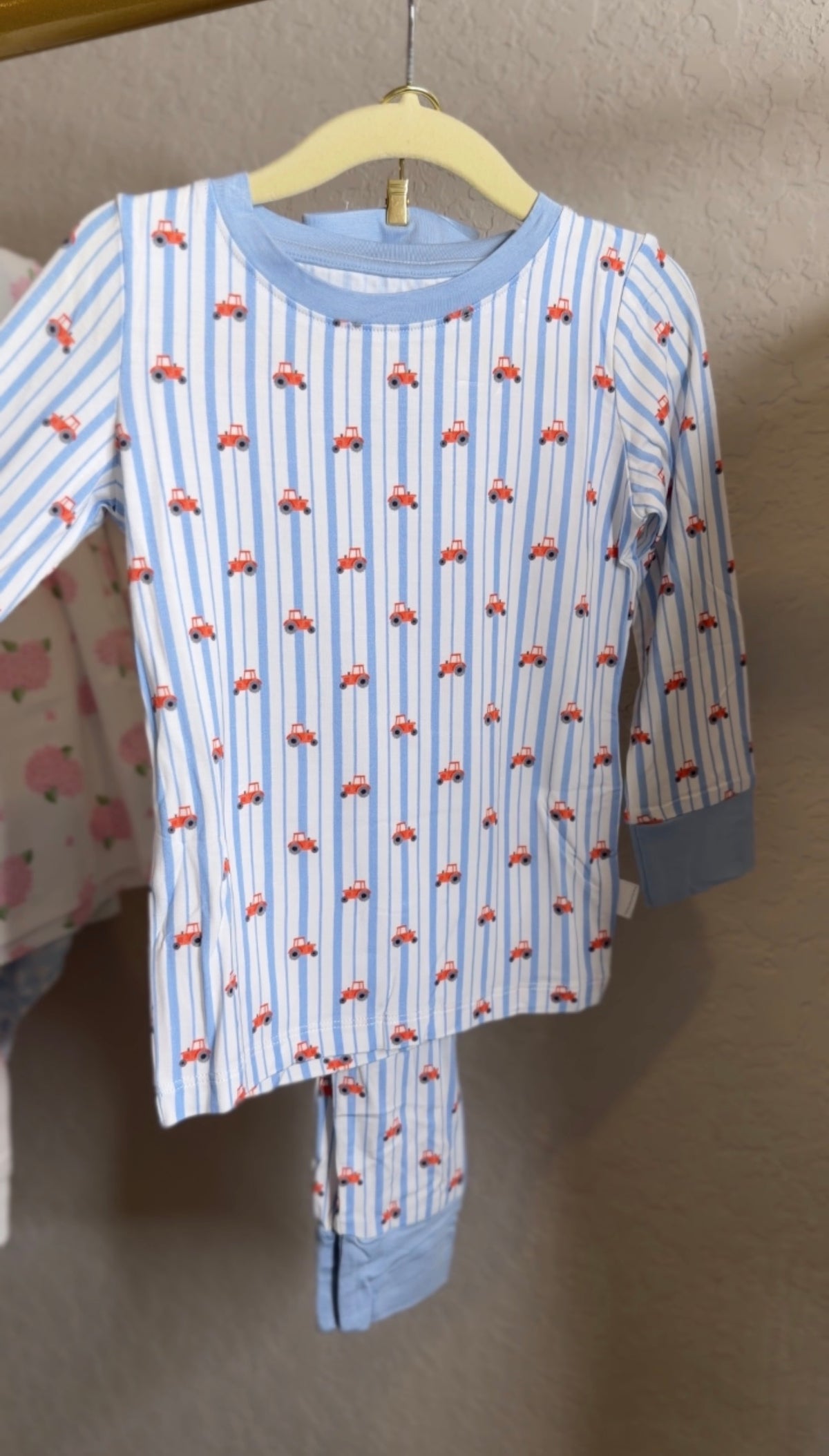 Children's pajama set with tractor pattern on a hanger against a neutral background