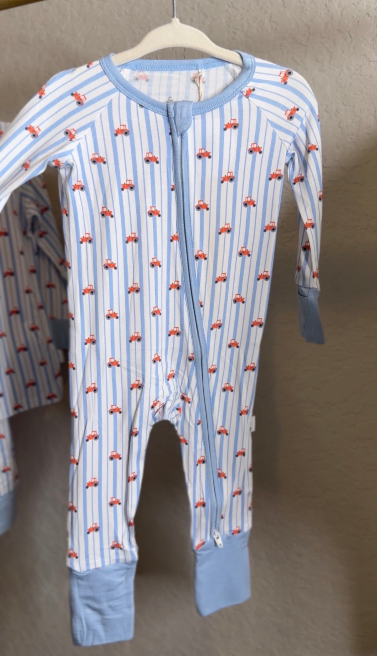 Children's onesie with red tractor and stripe pattern on a hanger against a neutral background