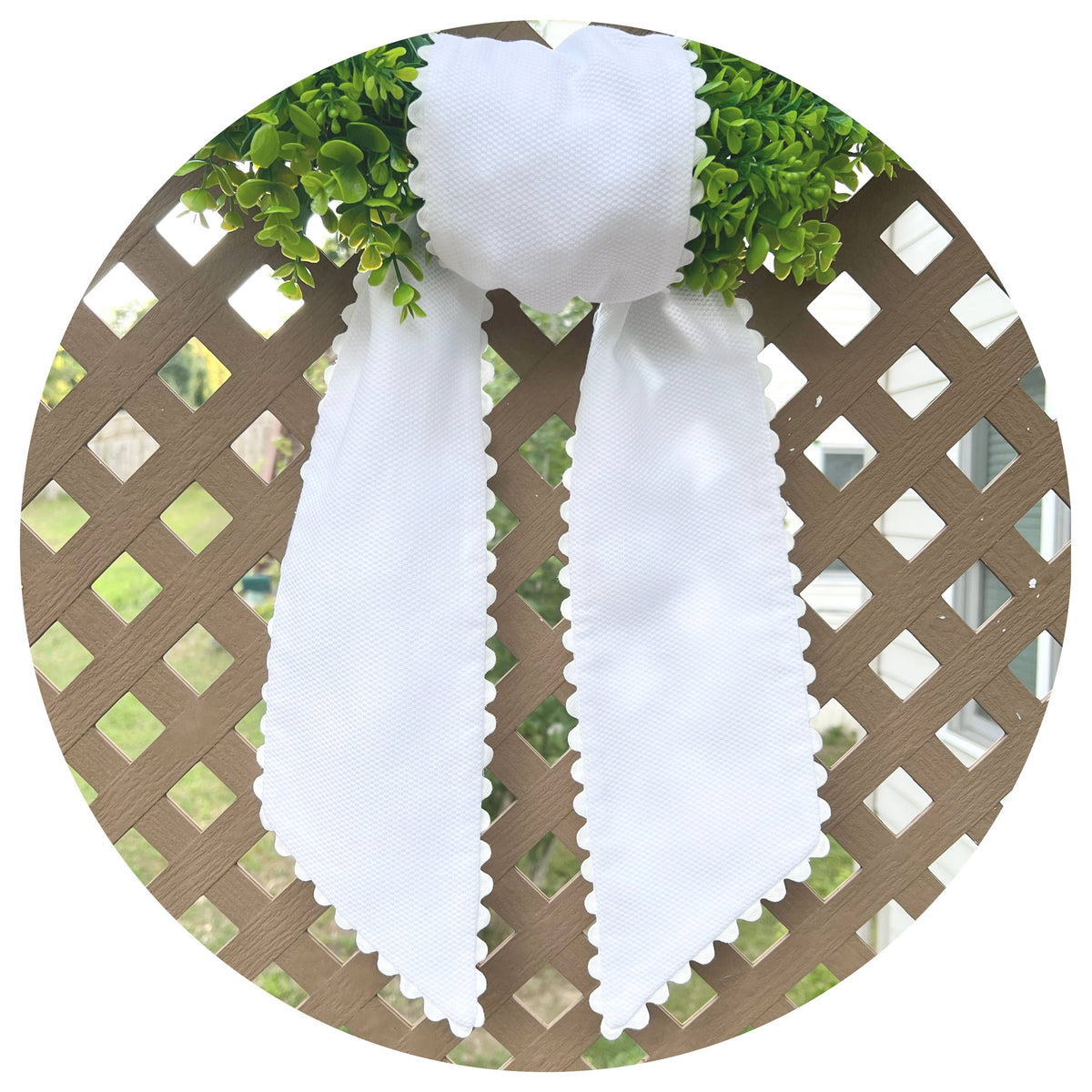 White decorative bow on a circular wreath with greenery against a lattice background