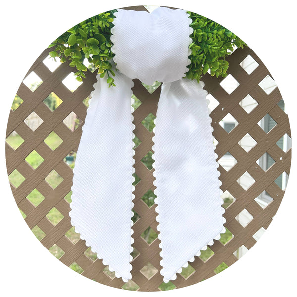 White decorative bow on a circular wreath with greenery against a lattice background