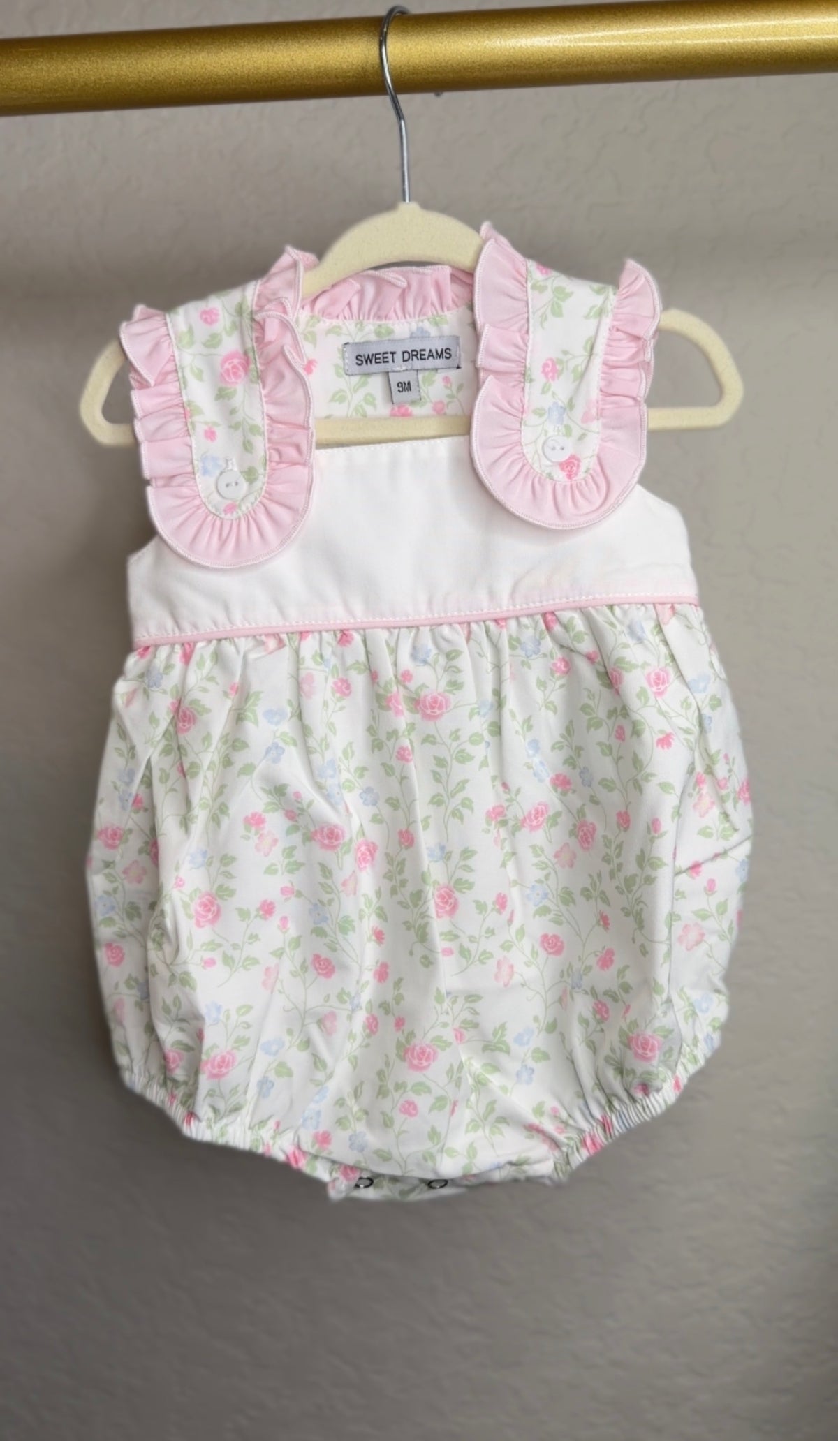 Baby romper with floral pattern and pink ruffled collar on a hanger.