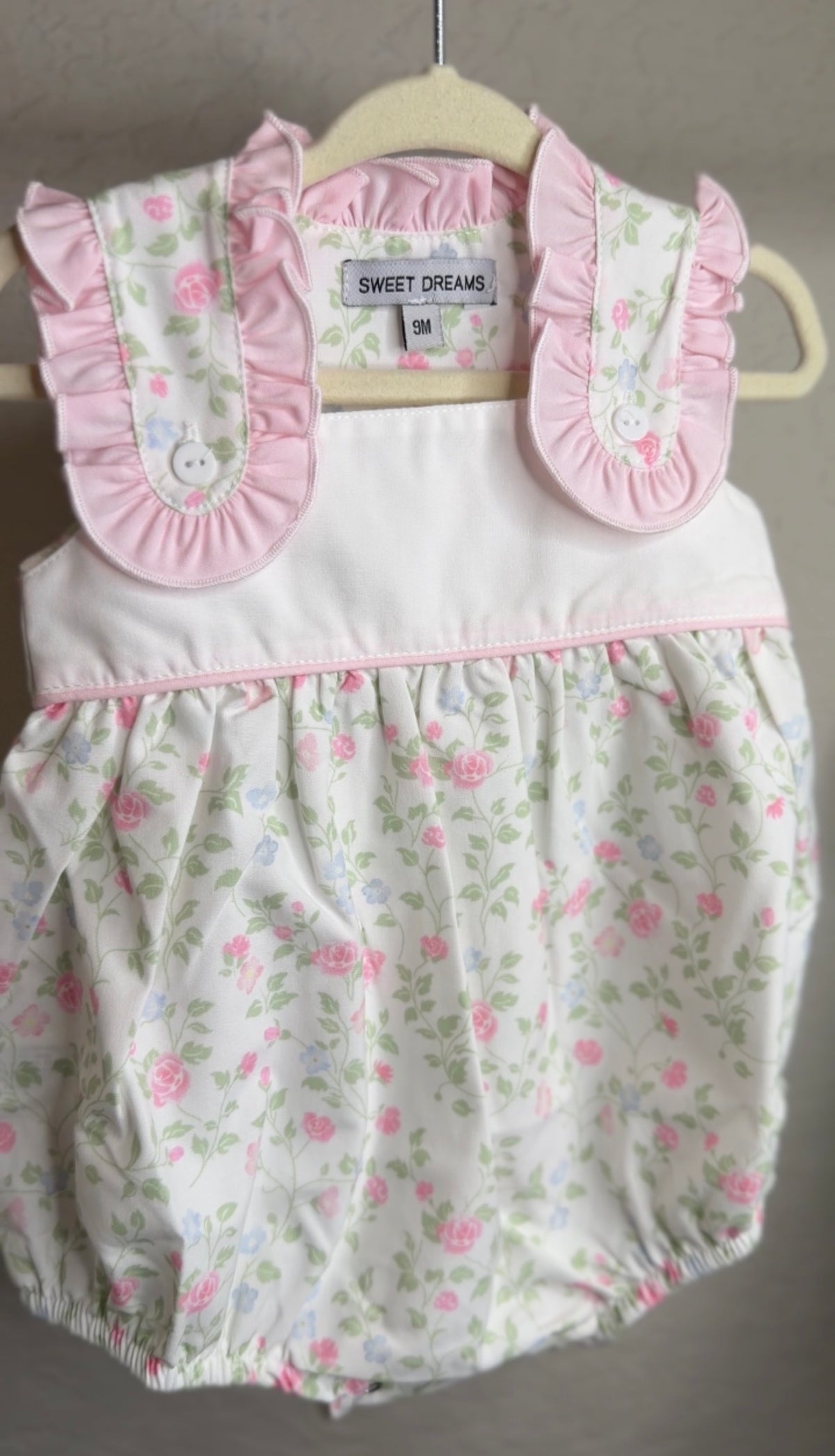 Baby romper with floral pattern and pink ruffled collar on a hanger.