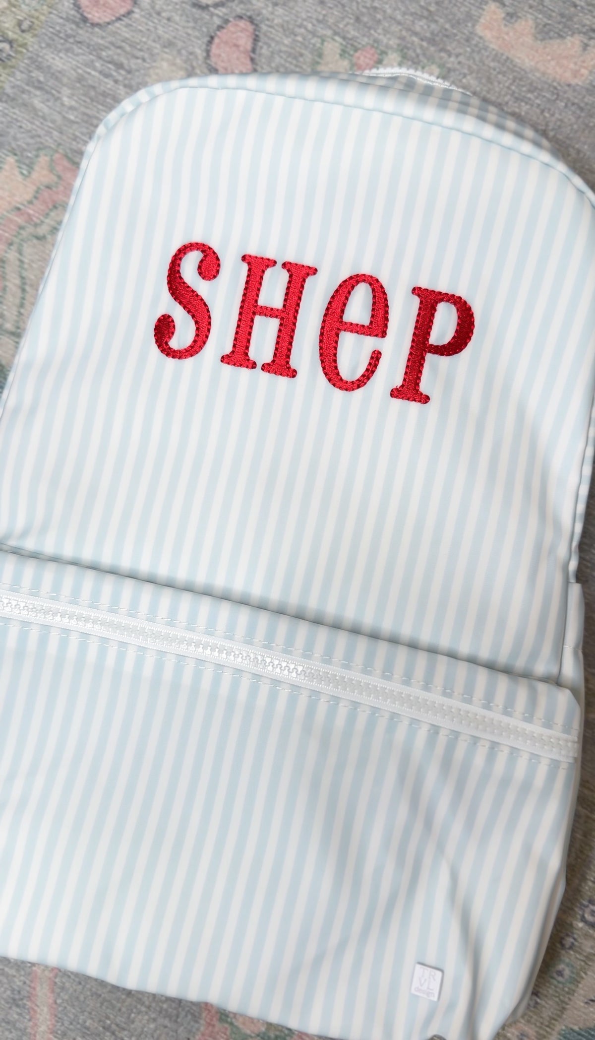 Light blue and white striped TRVL Backpacker embroidered with the red name 'Shep'