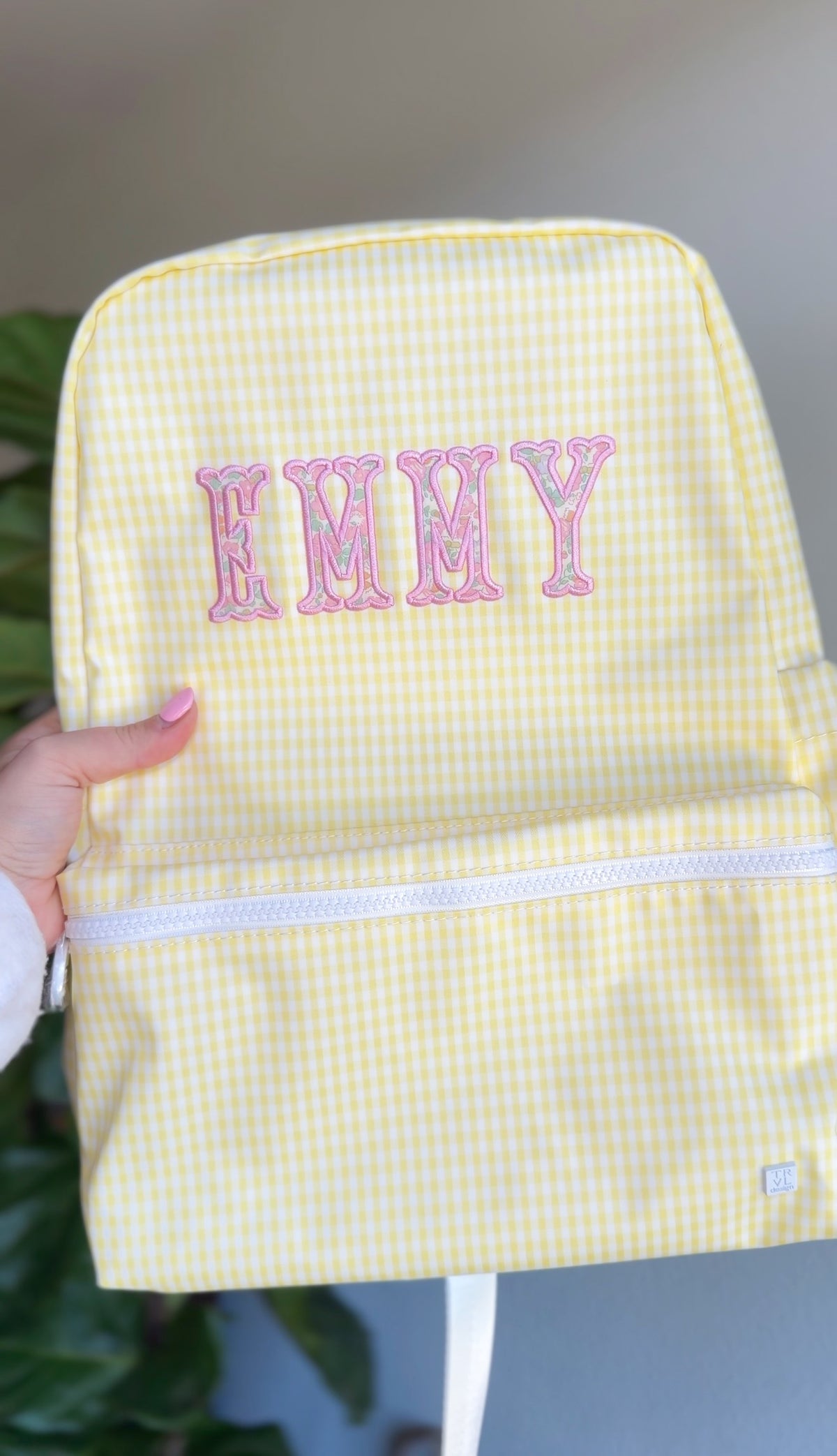Woman holding a yellow gingham TRVL Backpacker with pink embroidered name 'Emmy'