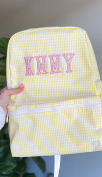 Woman holding a yellow gingham TRVL Backpacker with pink embroidered name 'Emmy'