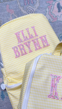 Yellow gingham TRVL Backpacker with pink embroidered name 'Elli Brynn', a second matching bag beside it