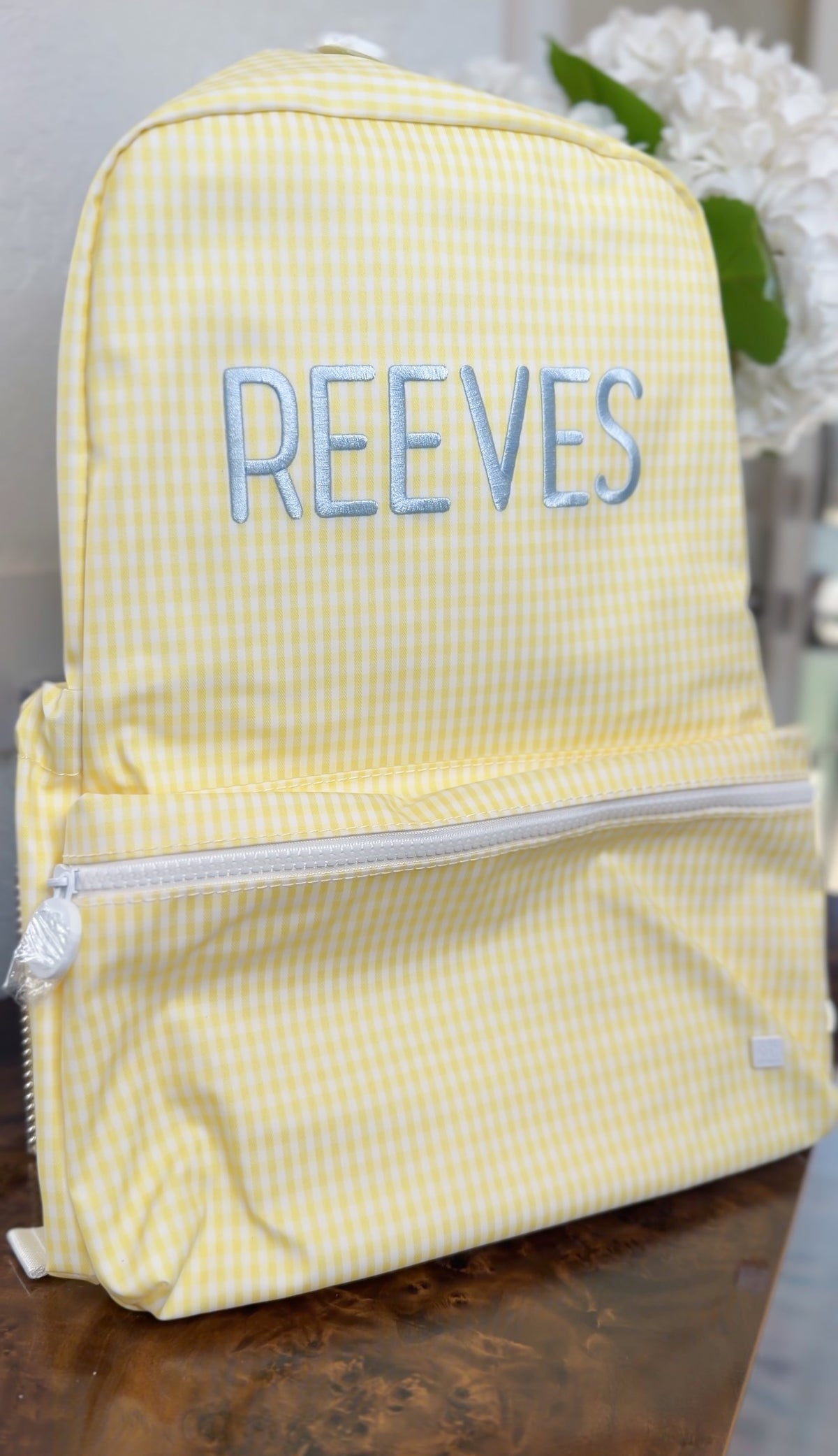 Yellow gingham TRVL Backpacker on a table with blue embroidered name 'Reeves'