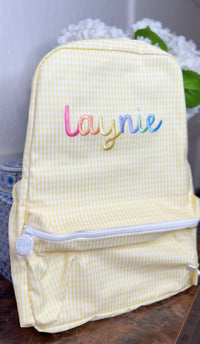 Yellow gingham TRVL Backpacker with rainbow-colored embroidered cursive name 'Laynie'
