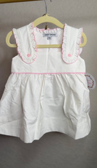 White with pink ruffle trim bloomer set hanging on a hanger in front of a blank wall