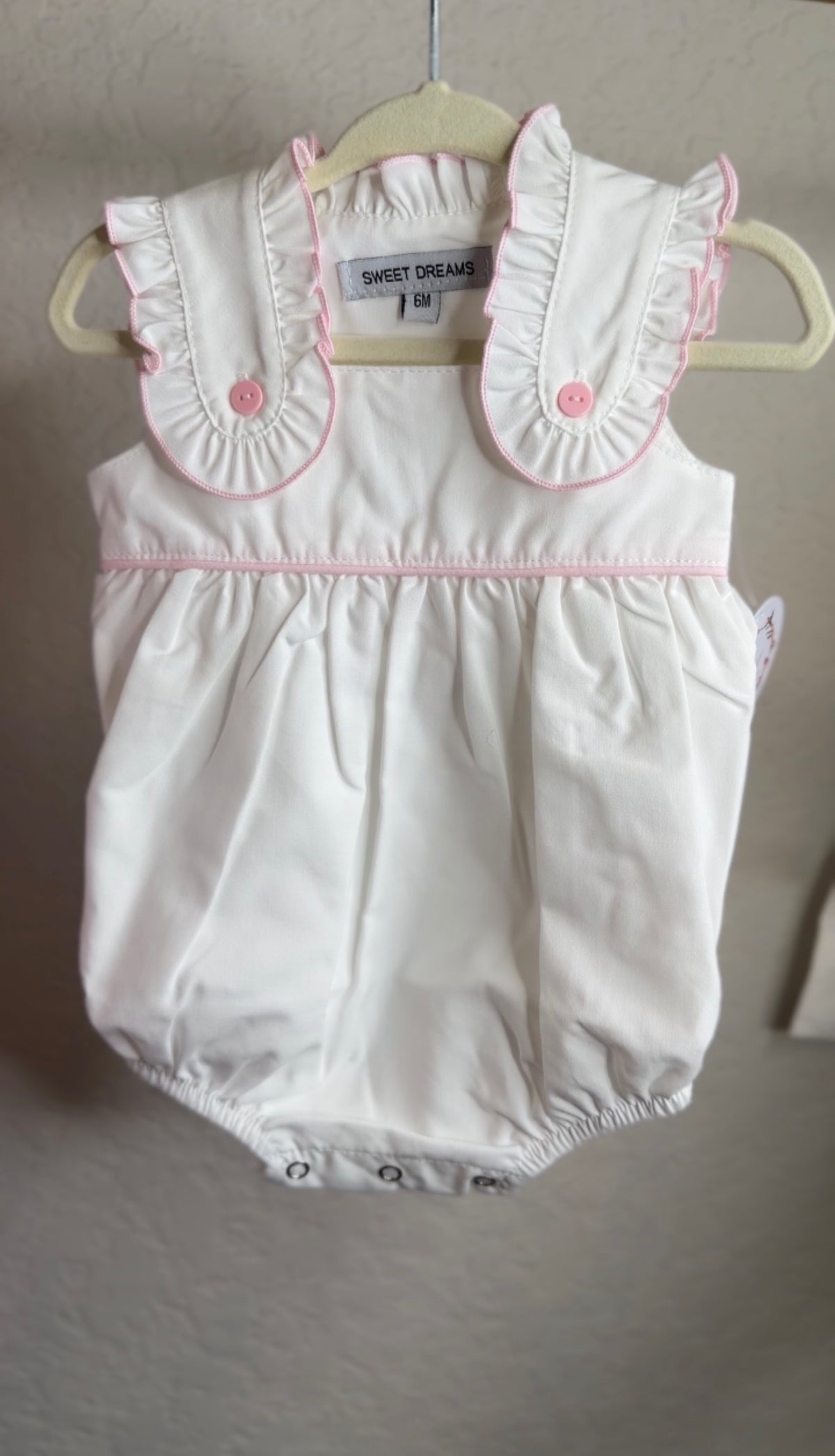 White baby romper with pink accents on a hanger against a neutral background