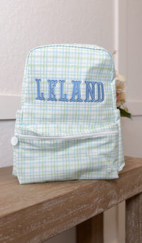 Green and blue plaid TRVL Backpacker embroidered with the name 'Leland'