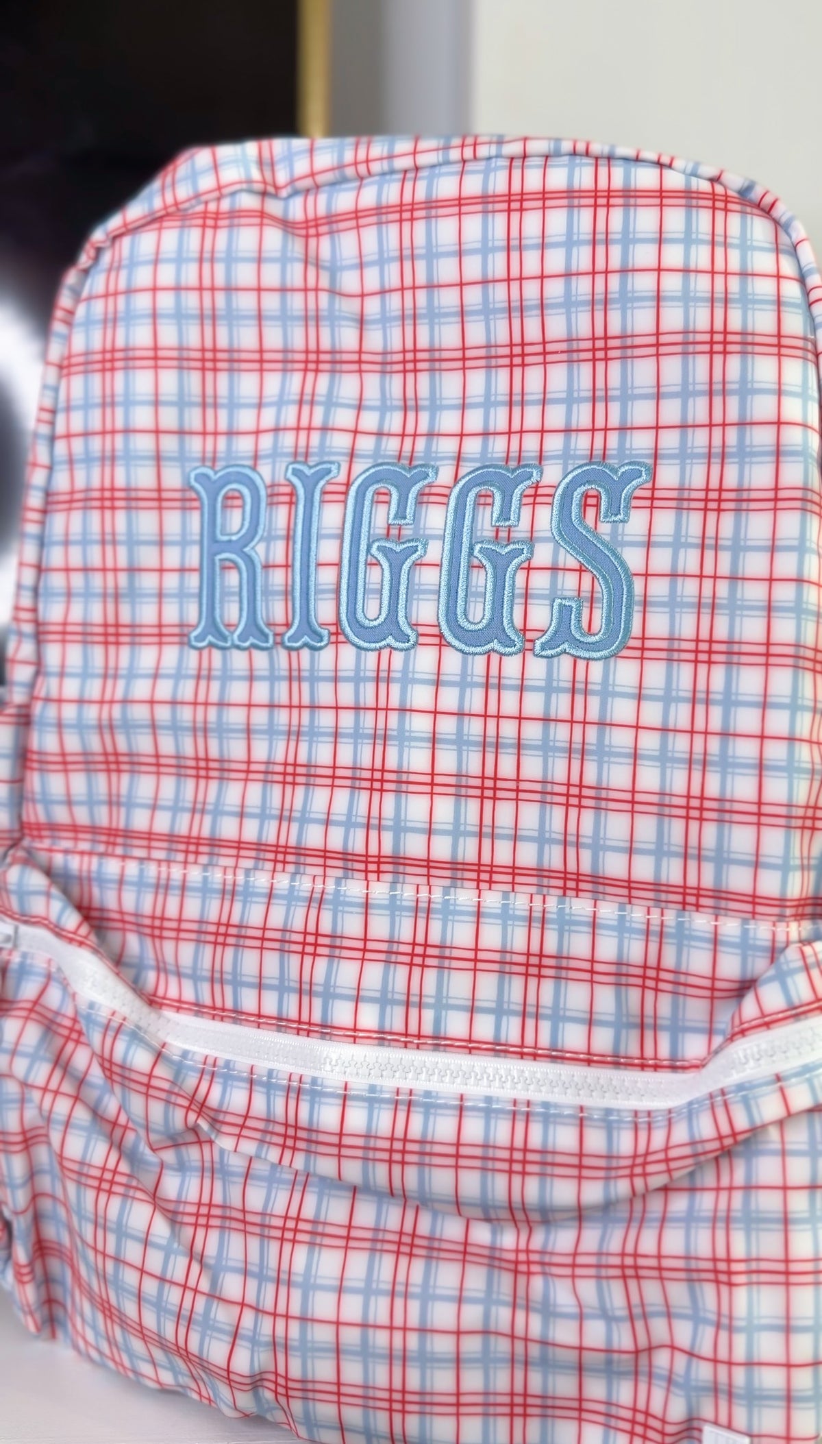 Red, white and blue plaid TRVL Backpacker embroidered with the name 'Riggs'