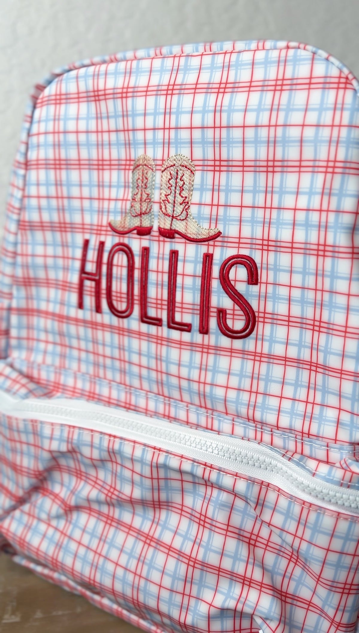 Red plaid TRVL Backpacker embroidered with cowboy boot icons and the name 'Hollis'