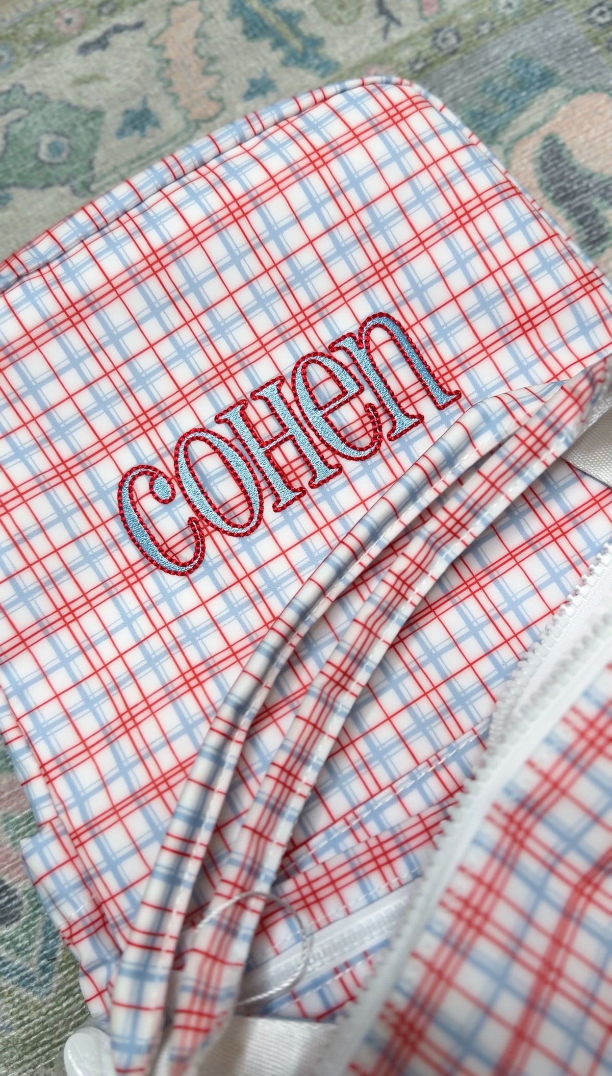 Red plaid TRVL bag embroidered with the name 'Cohen'