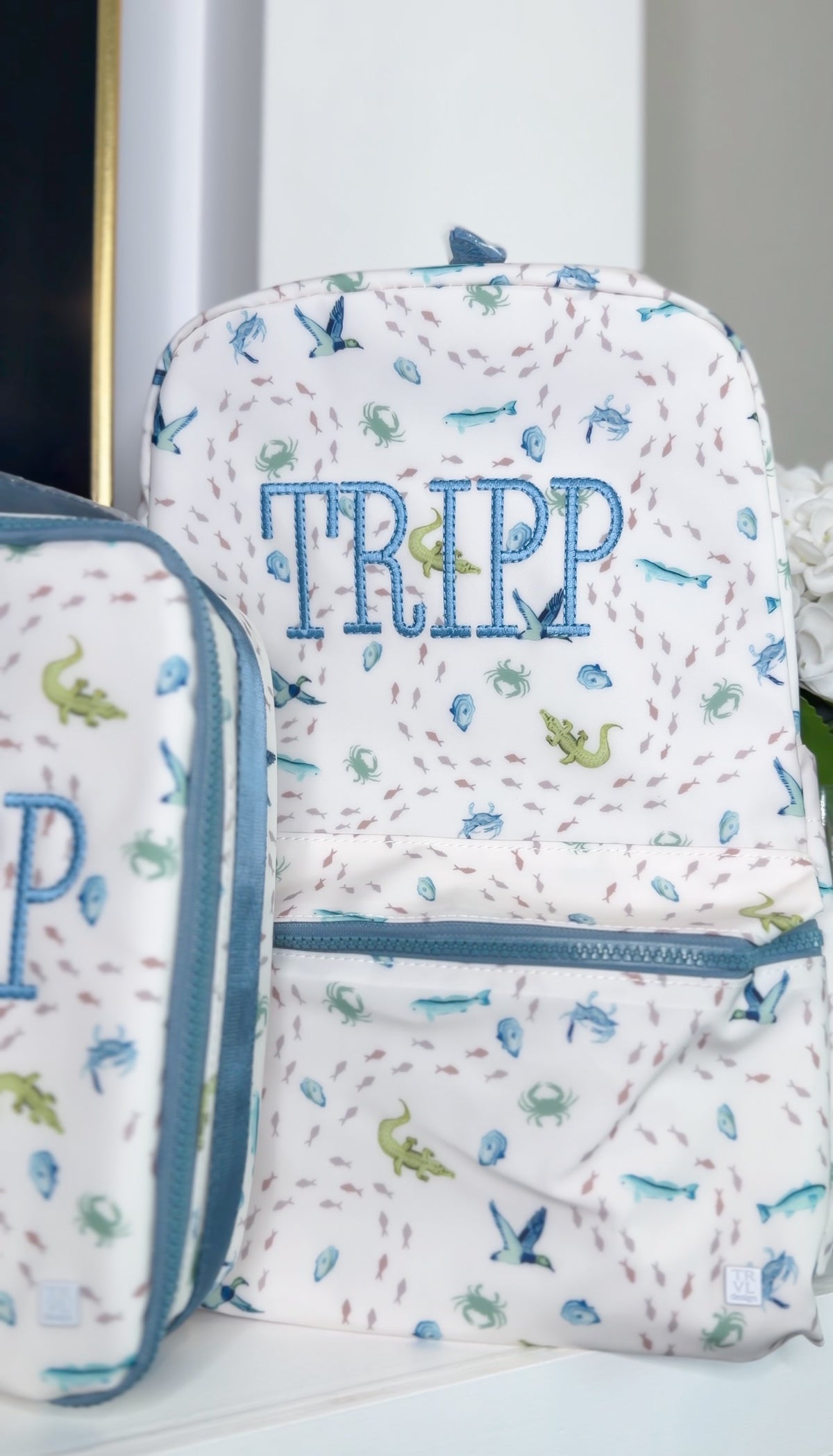 White TRVL Backpacker and pouch with blue coastal sea life print, embroidered with the name 'Tripp'