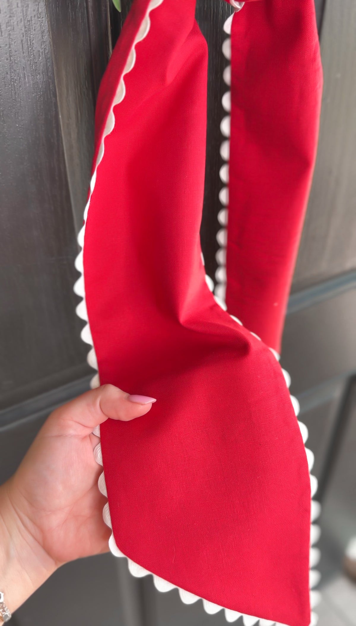 Red sash with white trim held by a hand against a neutral background
