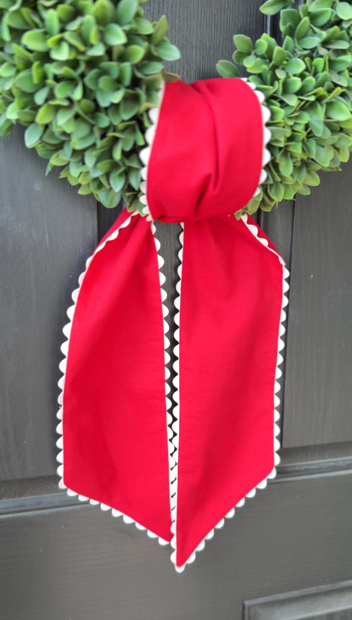 Red bow with white trim on a door with green wreaths.