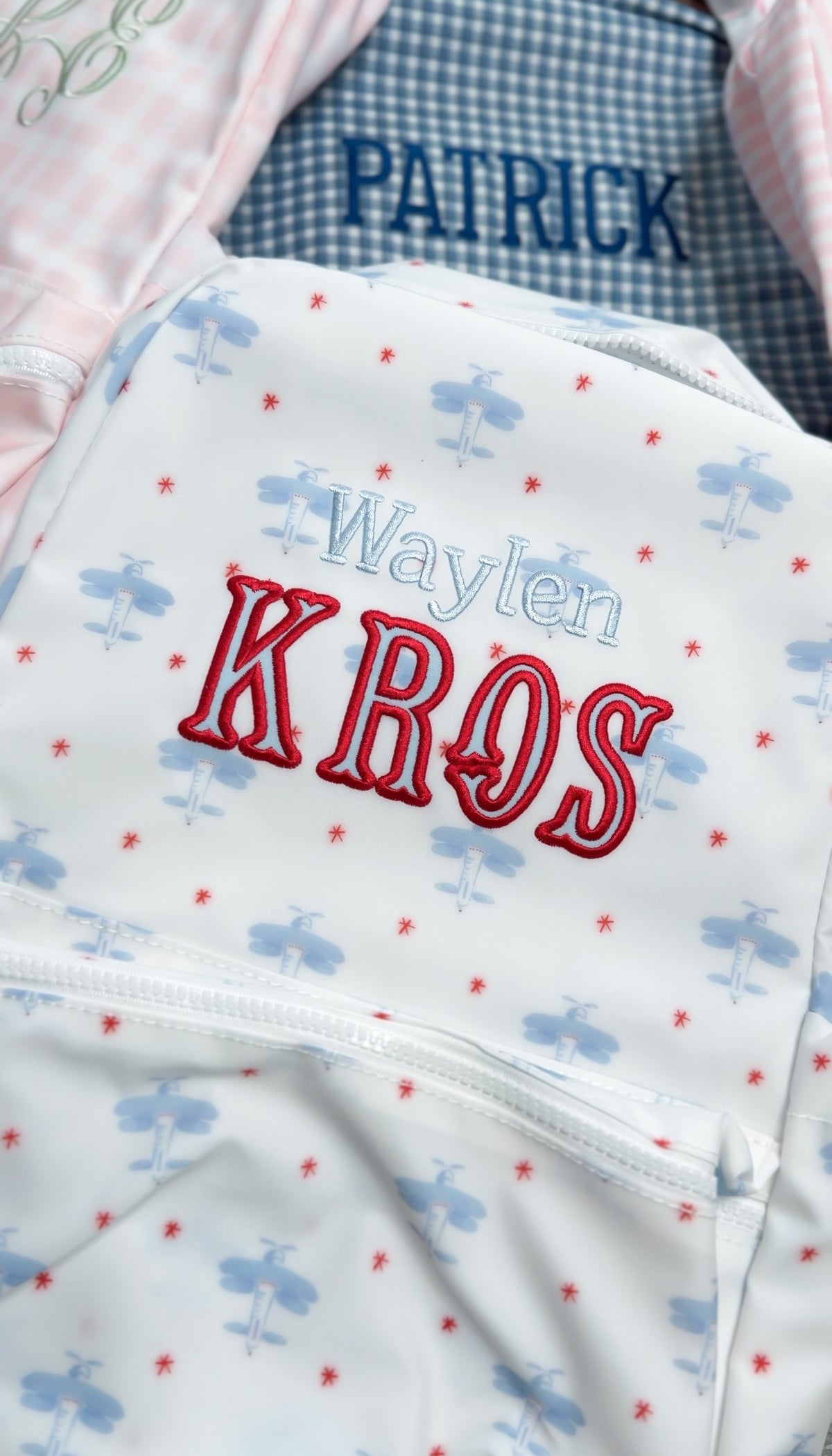 White TRVL bag with blue airplane print embroidered with the name 'Waylen Kros', next to a bag embroidered 'Patrick'