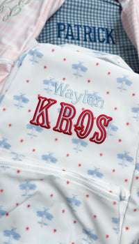 White TRVL bag with blue airplane print embroidered with the name 'Waylen Kros', next to a bag embroidered 'Patrick'