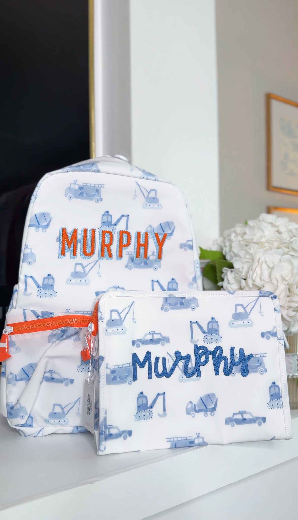 White TRVL Backpacker and pouch with blue construction truck print, embroidered with the name 'Murphy'
