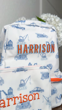 White TRVL Backpacker and pouch with blue construction truck print, embroidered with the name 'Harrison' in orange