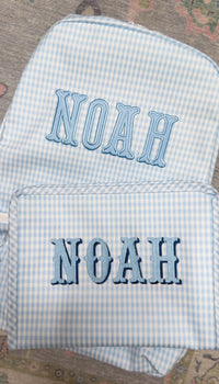 Light blue gingham TRVL Backpacker and pouch both embroidered with the name 'Noah'