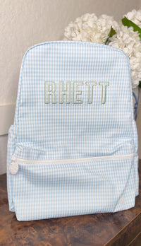 Light blue gingham TRVL Backpacker embroidered with the name 'Rhett'