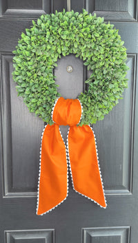 Green wreath with orange ribbon on a gray door