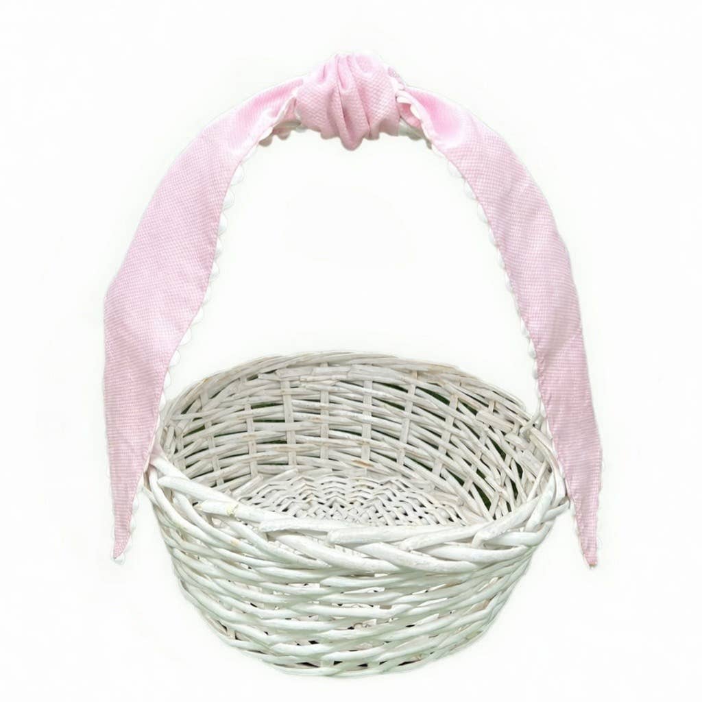 Pale pink cotton pique sash tied in a bow on the handle of a white wicker basket, plain background