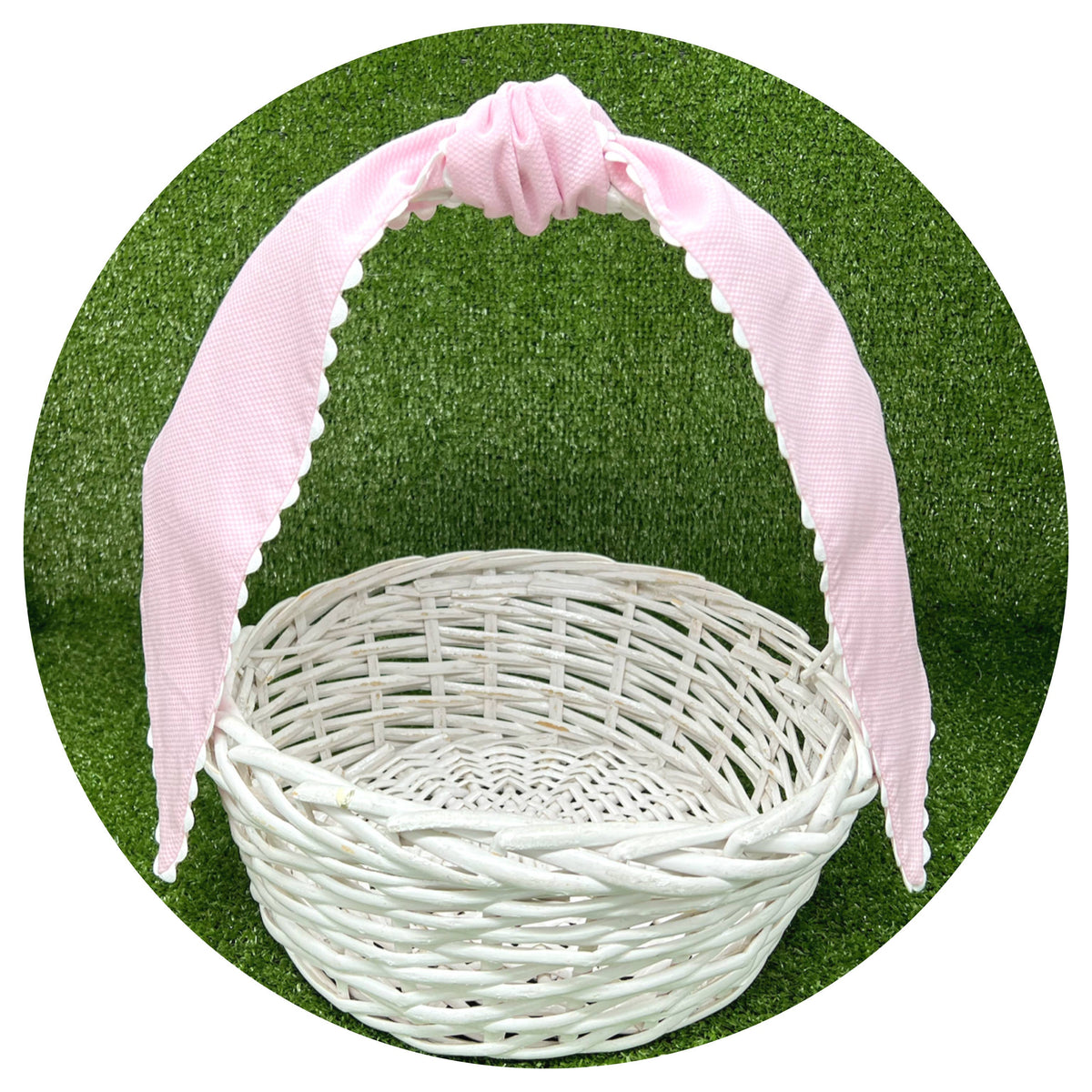 Pale pink cotton pique sash tied in a bow on a white wicker basket handle, styled against artificial turf