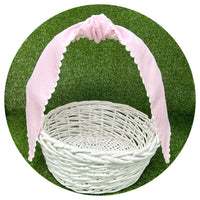 Pale pink cotton pique sash tied in a bow on a white wicker basket handle, styled against artificial turf