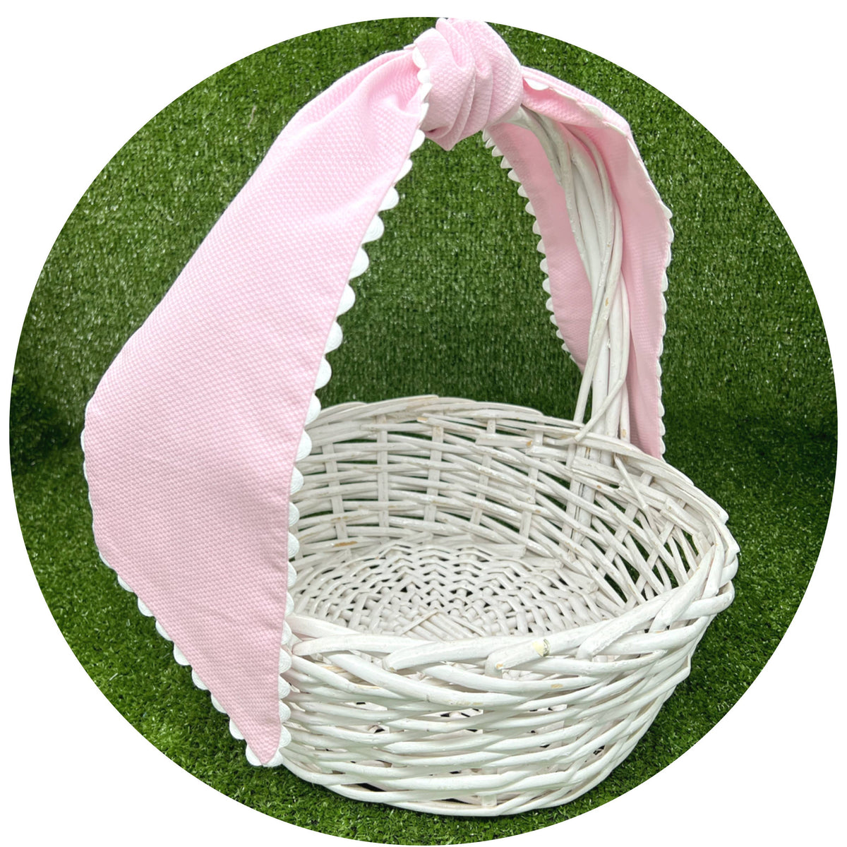 Pale pink cotton pique sash tied in a bow on a white wicker basket handle, side angle view against artificial turf