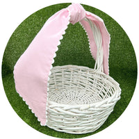 Pale pink cotton pique sash tied in a bow on a white wicker basket handle, side angle view against artificial turf