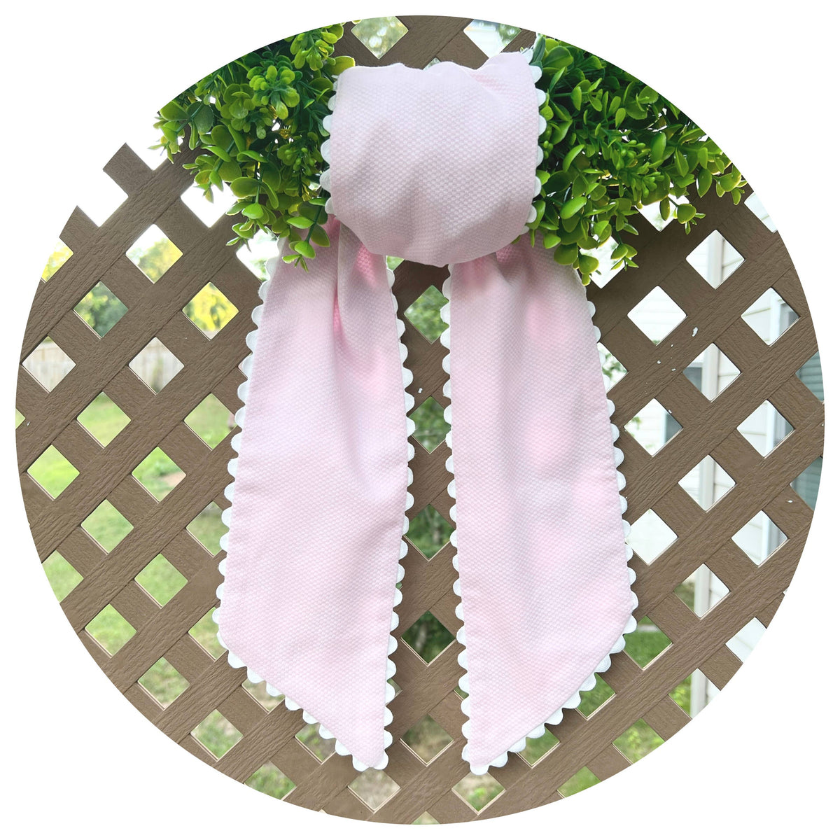 Pale pink cotton pique sash tied on a boxwood wreath, white scalloped trim, hung on a lattice backdrop