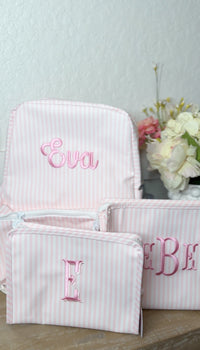 Pink and white striped backpack embroidered with the name 'Eva', next to matching pink striped pouches embroidered 'E' and 'B'