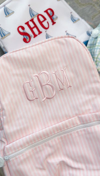 Pink and white striped backpack embroidered with a 'GBM' monogram in pink thread, close-up view