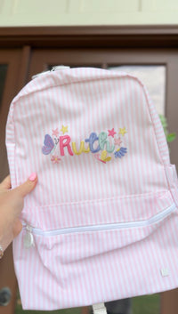 Pink and white striped backpack held up, embroidered with the name 'Ruth' in colorful lettering with butterflies and stars