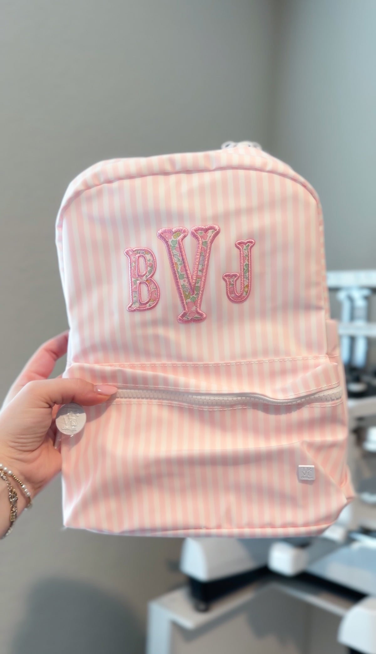 Pink and white striped backpack held up, embroidered with a 'BVJ' monogram in pink and floral thread